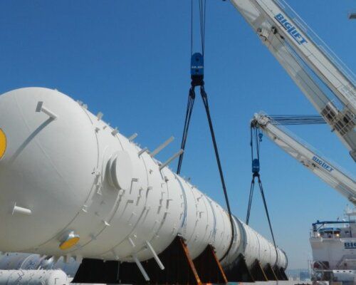 Large industrial vessel being lifted by cranes at a port